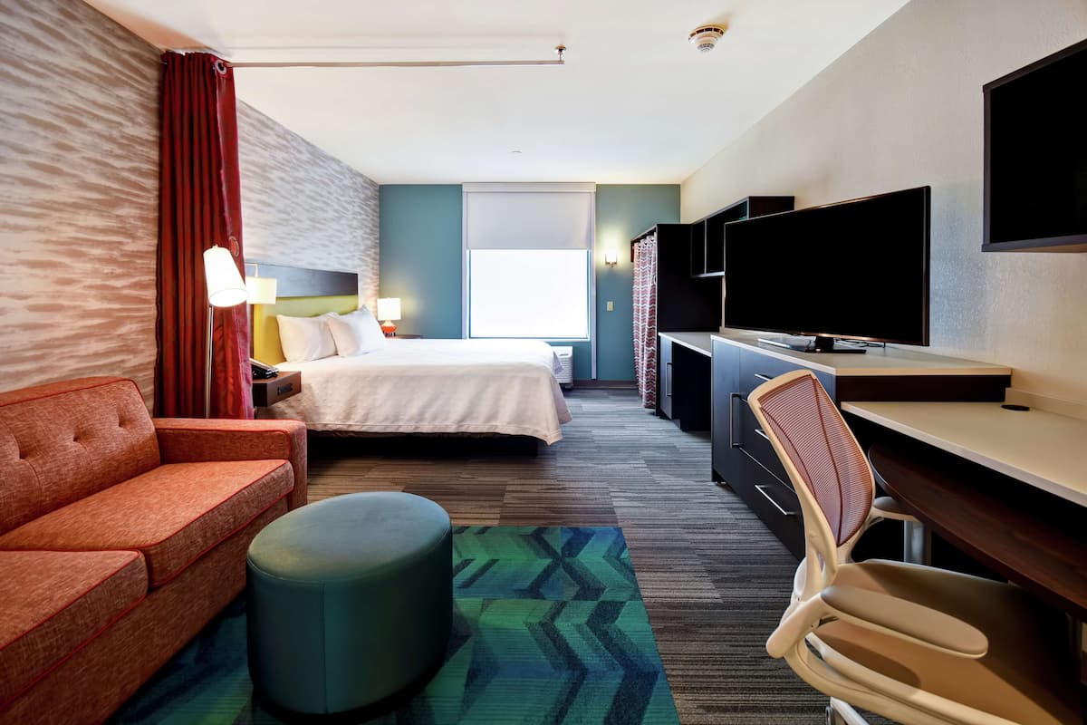 A hotel room with a bed, a sofa, a desk, a television, and a chair.