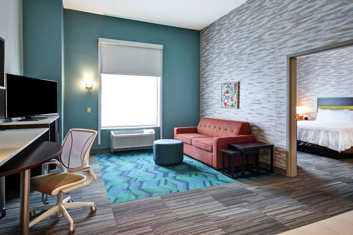 A modern hotel room with a desk, chair, sofa, ottoman, and a bed.