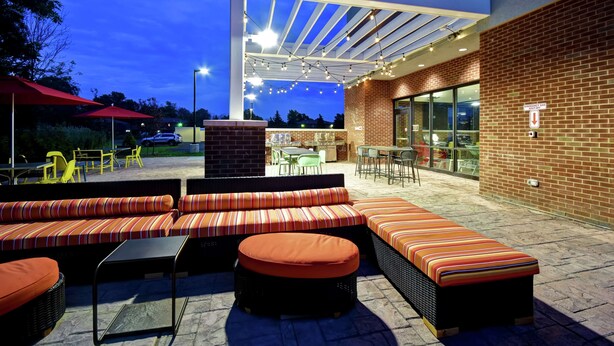 An outdoor seating area with a covered patio, brick walls, and a glass door entrance. - Home2 Suites by Hilton Amherst Buffalo (Buffalo)