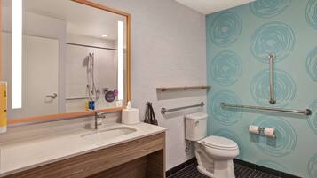 A modern bathroom with a sink, mirror, toilet, and handrails.