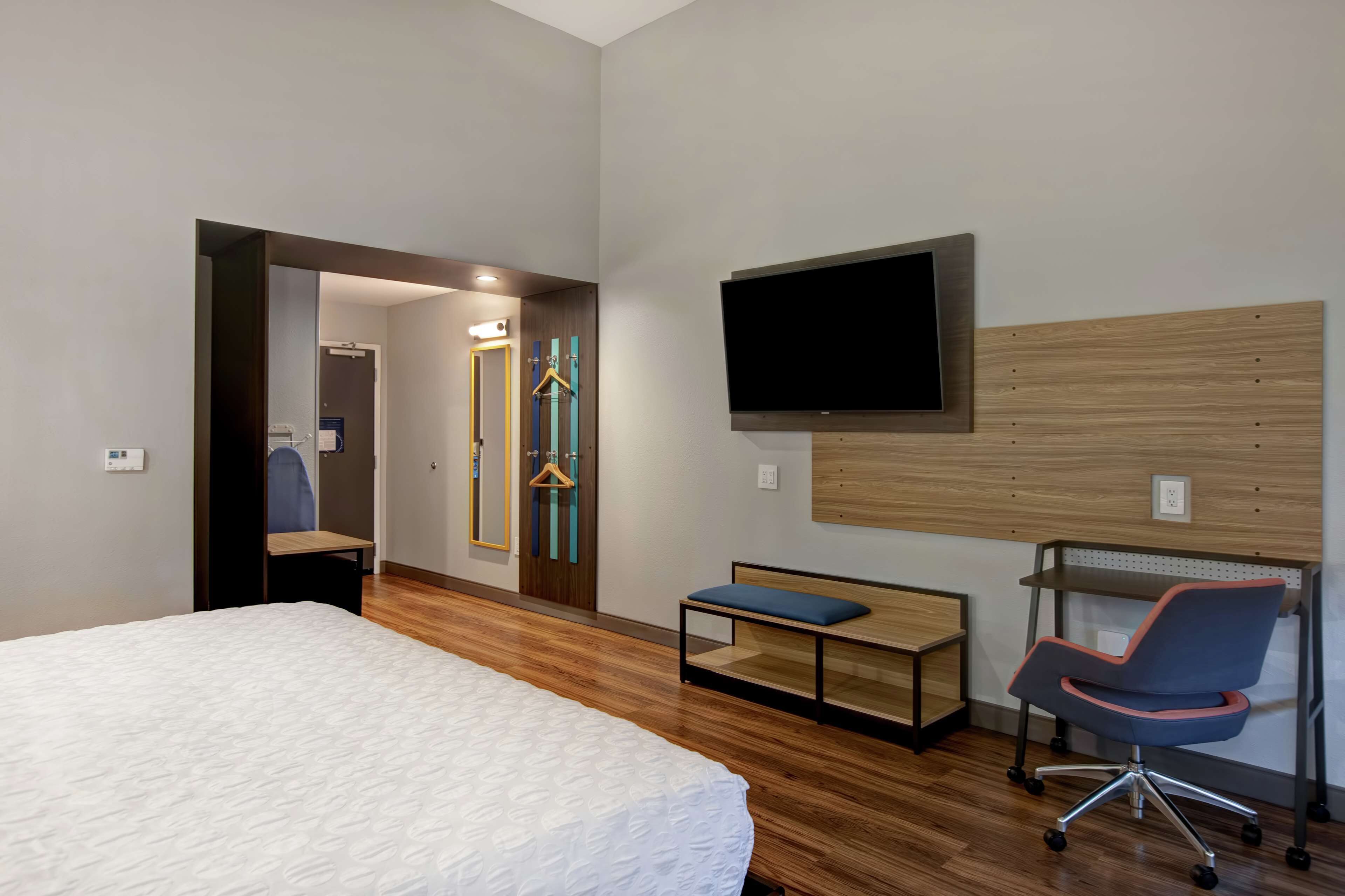 Habitación de hotel con una cama grande, un escritorio con silla, un televisor montado en la pared y un espejo con marco de madera.