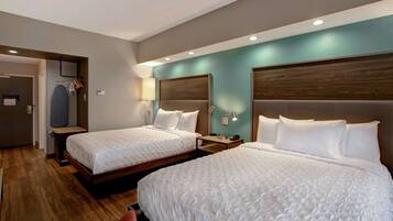 Habitación de hotel con dos camas, suelo de madera, una pared de acento color verde azulado y cabecero de madera.