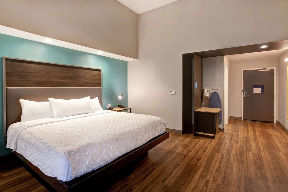 A modern hotel room with a large bed, a nightstand, a small table, and a chair.