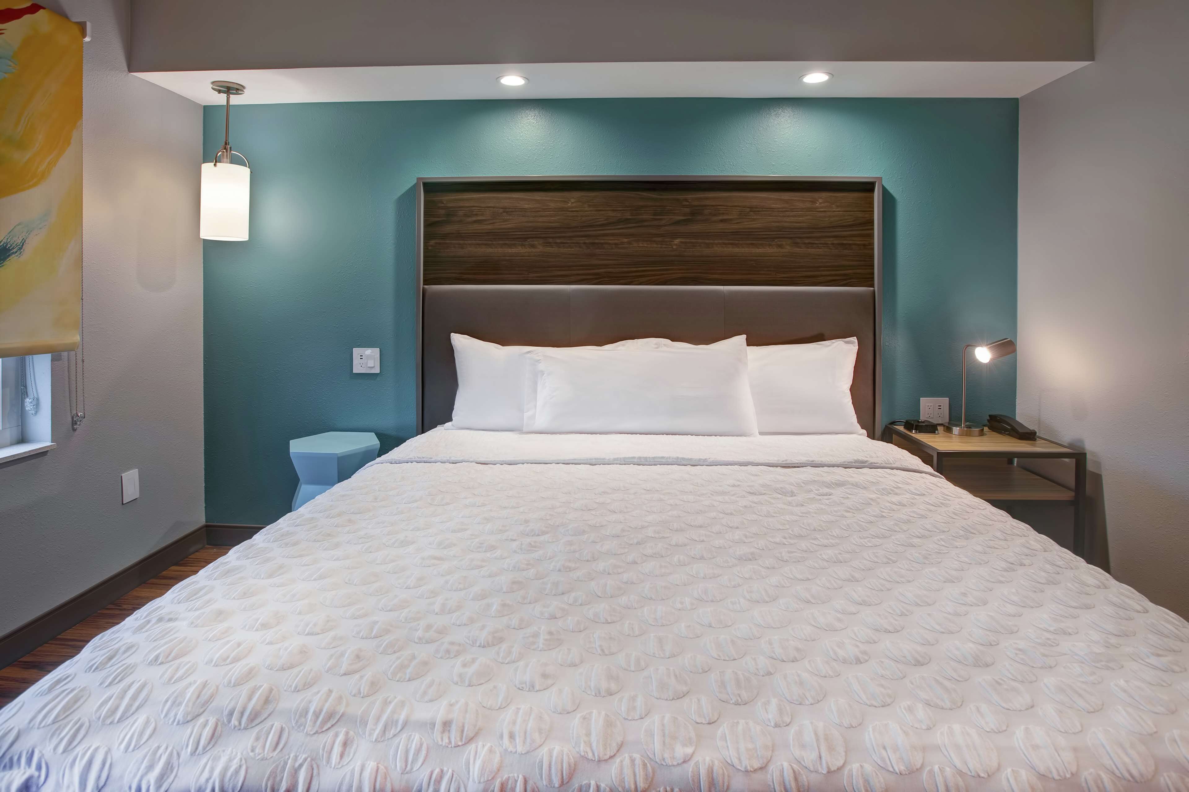 A neatly made bed with a white duvet and pillows, a wooden headboard, and a small bedside table with a lamp.