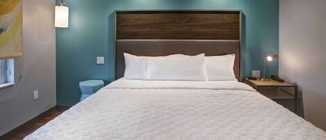 A neatly made bed with a white duvet and pillows, a wooden headboard, and a small bedside table with a lamp.