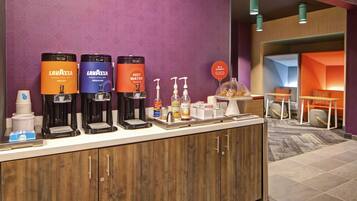 Et hotelreceptionsområde med kaffestation, inklusive Lavazza espressomaskiner, en selvbetjeningsstation til drikkevarer og et lille siddeområde med en glaskuppeldisk.