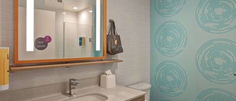 A bathroom with a sink, mirror, and toilet. There is a towel rack and a bag hanging on the wall.