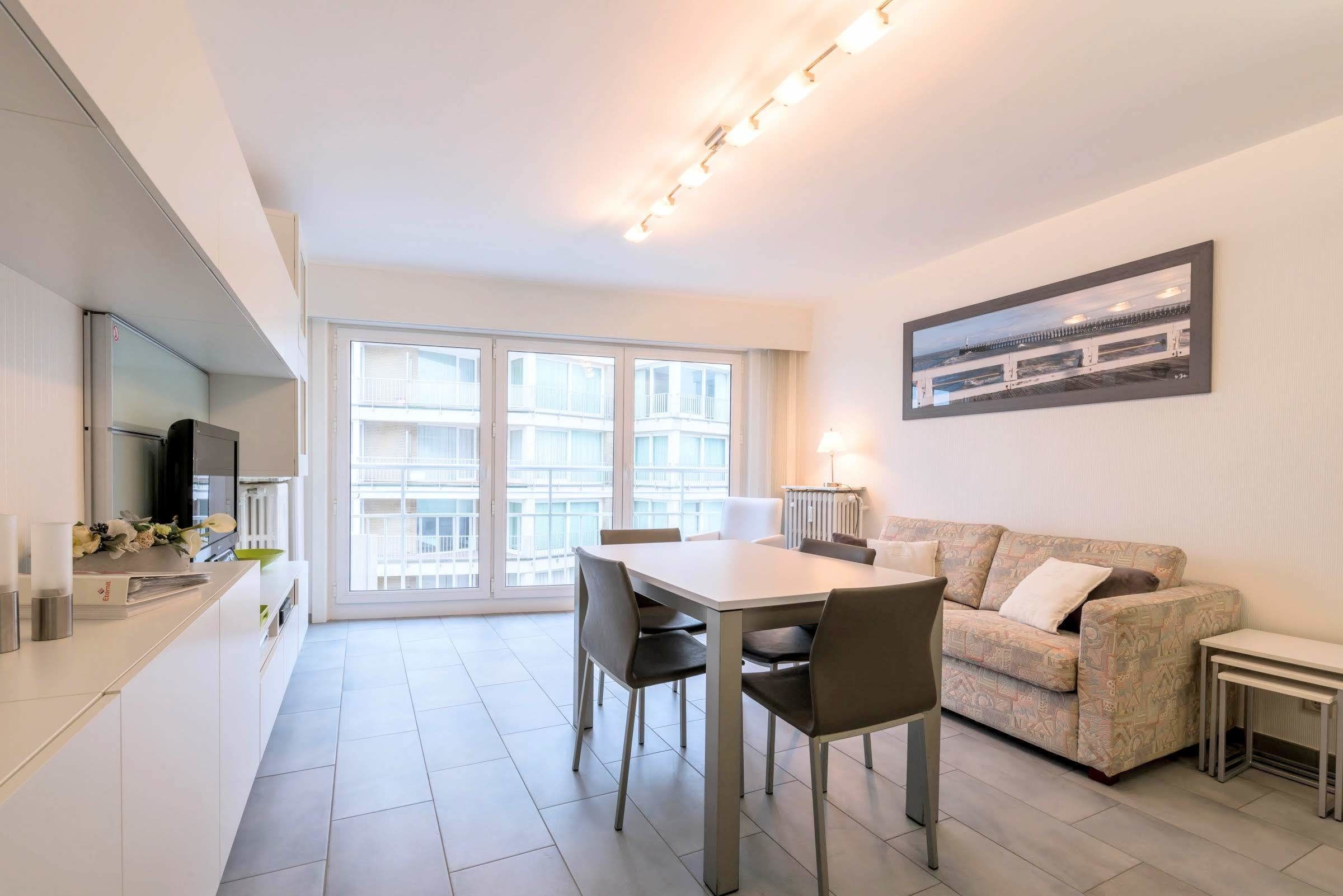 A modern kitchen with a dining area, a sofa, and a large window.