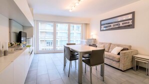 A modern kitchen with a dining area, a sofa, and a large window. - Nevada 3-4 (Koksijde)