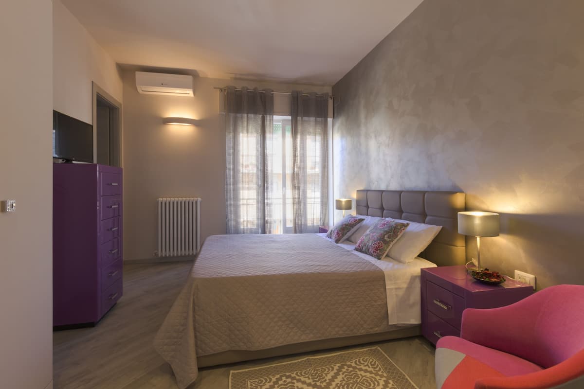 A bedroom with a bed, a nightstand with a lamp, a dresser, and a chair.