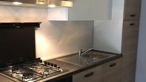 A modern kitchen with a gas stove, oven, and stainless steel sink. - B&B Da Peo (Porto San Giorgio)
