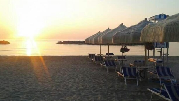 A beach with rows of sun loungers and thatched umbrellas, a calm sea, and a small island in the distance. - B&B Da Peo (Porto San Giorgio)