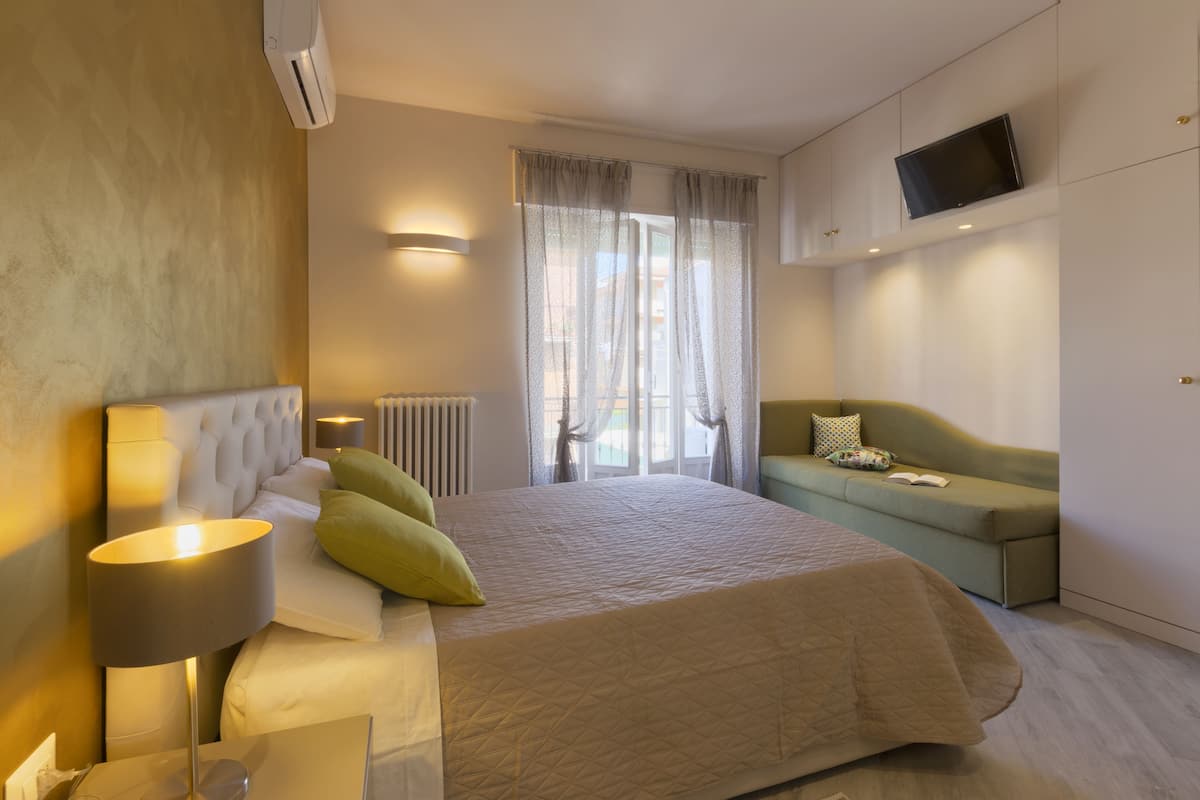 A modern hotel room with a large bed, a sofa, a flat-screen TV, and a window with curtains.