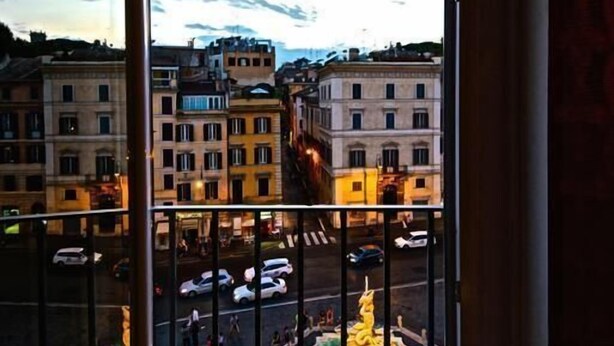 A view through a window with a balcony, overlooking a cityscape with buildings and a fountain. - Penthouse Suite Rome (Rome)