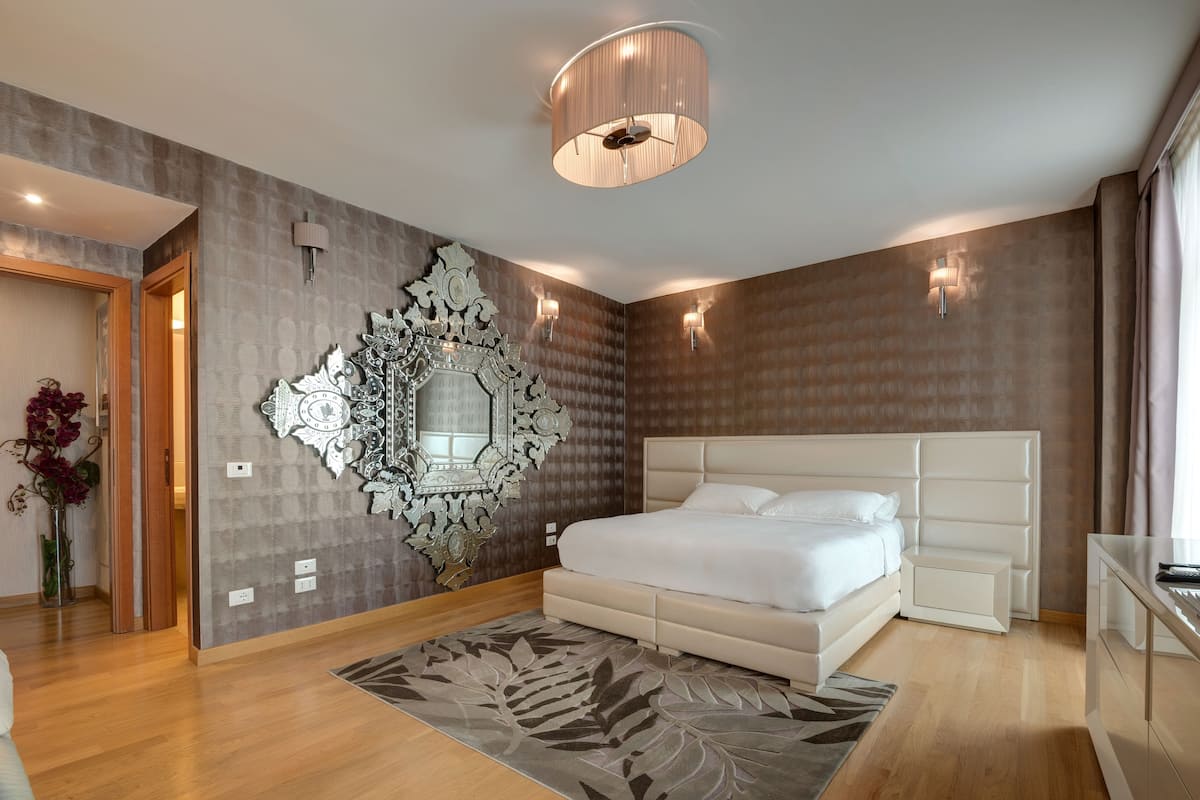 A modern bedroom with a large bed, a decorative mirror, and a unique wall design.