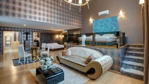 A modern hotel room with a curved sofa, a dining area with a glass table, and a staircase. - Penthouse Suite Rome (Rome)
