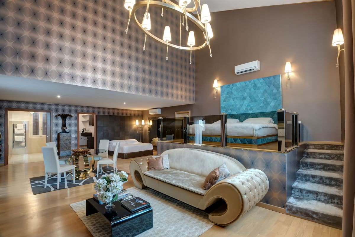 A modern hotel room with a curved sofa, a dining area with a glass table, and a staircase.