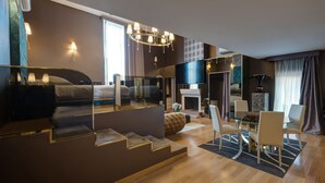 A modern hotel room with a large bed, a glass partition, a dining area with a table and chairs, and a fireplace. - Penthouse Suite Rome (Rome)