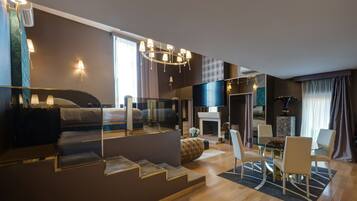 Una habitación de hotel moderna con una cama grande, un separador de vidrio, un área de comedor con mesa y sillas, y una chimenea.