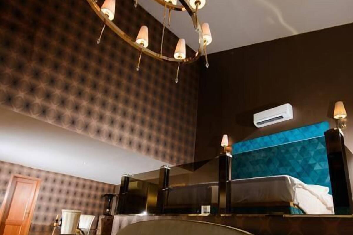 A modern hotel room with a unique curved sofa, a chandelier, and a blue accent wall.
