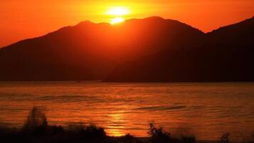 Um pôr do sol sobre a água, com montanhas ao fundo.