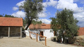 A stone building with a red-tiled roof, a wooden staircase, and a large tree in the background. - Casa de Santa Cristina (Marco de Canaveses)