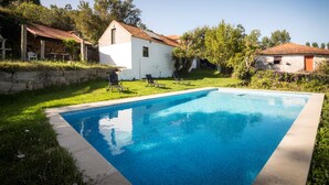 A rectangular swimming pool with a stone wall and a white building with a red roof in the background. - Casa de Santa Cristina (Marco de Canaveses)