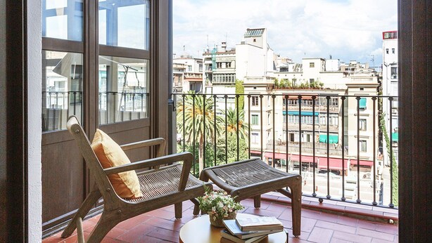 A balcony with a wooden bench and a table, overlooking a cityscape with buildings and a clear sky. - Weflating City Center (Barcelona)