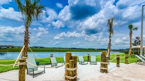 A waterfront patio with lounge chairs and a rope barrier, overlooking a lake and palm trees. - Storey Lake 4 Bedroom Townhome w Splashpool - 1624ST (Kissimmee)