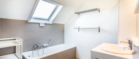 Un baño moderno con tragaluz, una bañera, un lavamanos y un perchero para toallas.
