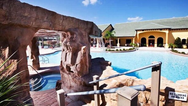 A pool area with a rock formation, a sign prohibiting climbing on rocks, and a building with a tiled roof in the background. - 3205pp (Kissimmee)