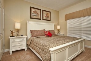 A bedroom with a large bed, two bedside tables, a nightstand, a dresser, and a window with blinds.