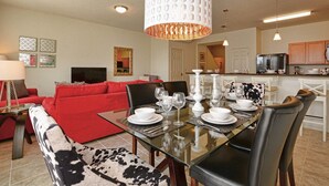 Una sala de estar moderna con un sofá rojo, una mesa de comedor de vidrio preparada para cuatro comensales y una cocina al fondo.