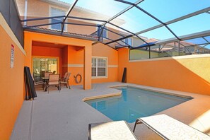 Una piscina interior con techo de vidrio, paredes color naranja y un área de estar con sillas y una mesa.