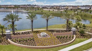 A golf course with a pond, palm trees, and a sign for Solara Resort. - Solara 9 Bedroom House w Pool - 8100SA (Kissimmee)