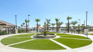 A landscaped area with a central fountain, surrounded by trimmed grass and palm trees.