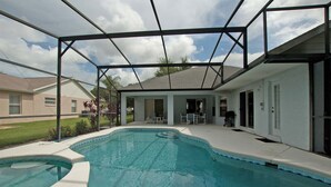 A swimming pool with a covered patio area, a lawn, and a house in the background. - Greater Groves 4 Bedroom Home w Pool - 5204GG (Clermont)