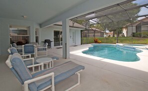 Un espacio al aire libre techado con piscina, sillones de descanso y una parrilla.