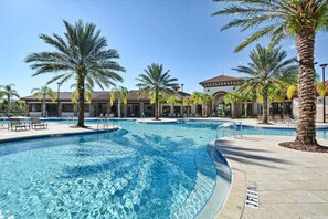 Une piscine bordée de palmiers, avec des chaises longues et, au fond, un bâtiment doté d’un toit recouvert de tuiles.