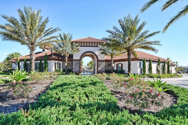A two-story building with a central arched entrance, surrounded by palm trees and landscaped gardens.