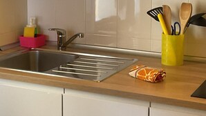 Una cocina con un lavamanos de acero inoxidable, un microondas y un utensilero amarillo sobre la encimera.