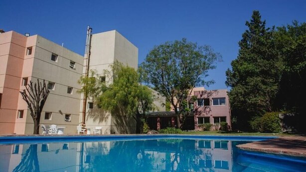 A swimming pool with a clear blue water surface, surrounded by buildings and trees. - Convivir Departamentos (Córdoba)