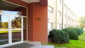 A building with a red facade, large glass doors, and a tiled entrance area. - Convivir Departamentos (Córdoba)