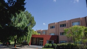A modern building with a red-brick entrance, surrounded by trees and a clear sky. - Convivir Departamentos (Córdoba)