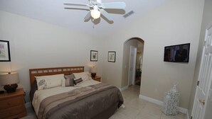 Ein Schlafzimmer mit einem Bett, Nachttischen, einem Deckenventilator, einem Fernseher und einer Tür zu einem anderen Raum.