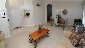 Een ruime woonkamer met een houten salontafel, een eethoek met een kroonluchter, en een gezellige zithoek met gestreepte kussens.