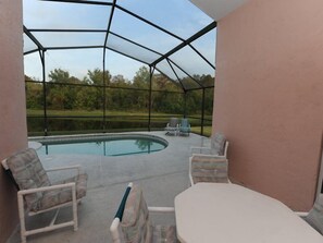 A covered outdoor area with a pool, chairs, and a table. - Indian Point 00 (Kissimmee)