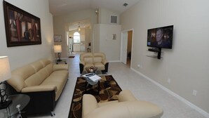 A living room with a beige sofa, a coffee table, and a TV mounted on the wall. - Indian Point 00 (Kissimmee)