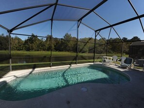 A swimming pool with a covered area, surrounded by chairs and a view of a lake and trees. - Indian Point 00 (Kissimmee)