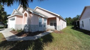 A single-story house with a pink facade, a brick foundation, and a small front yard with a palm tree. - Indian Point 00 (Kissimmee)